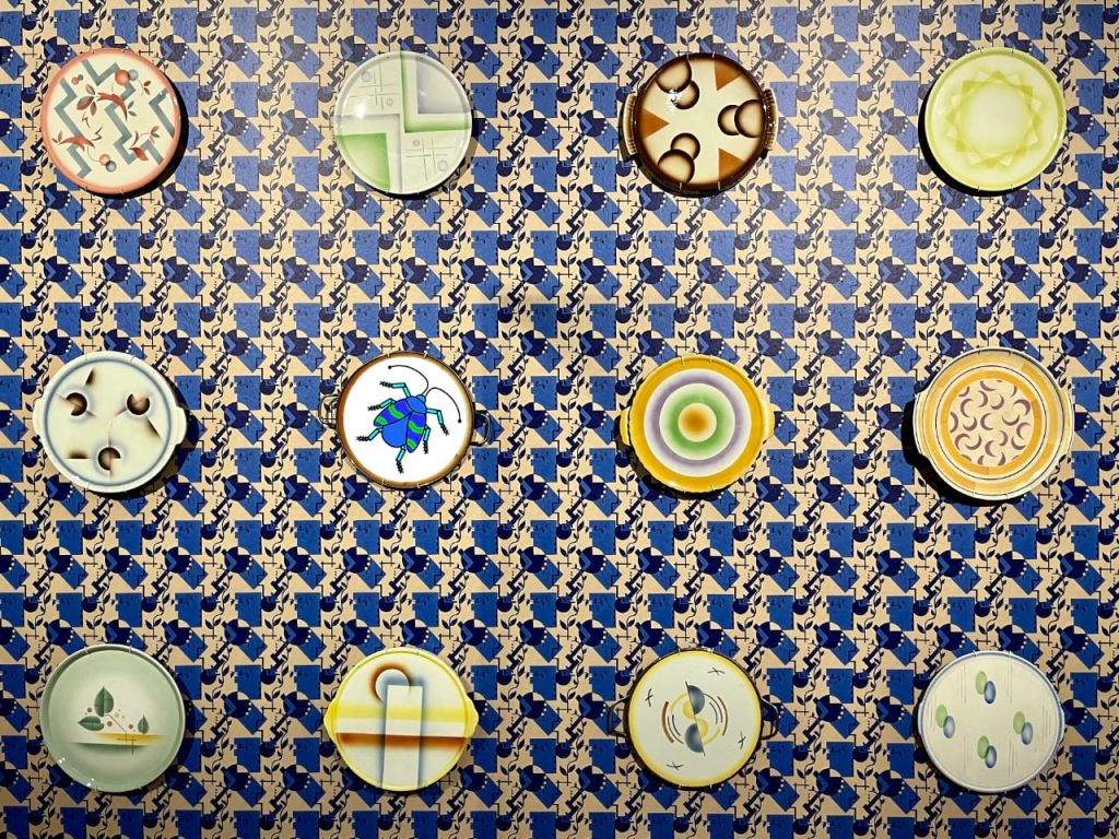 Das Folgenbild der 33. Folge des museumbug-Podcast. Eine im Stil der Zwanziger Jahre gestaltete blau-besche Tapete. An der Wand sind Teller mit unterschiedlichen Mustern angebracht. Auf einem ist das museumbug-Logo zu sehen.